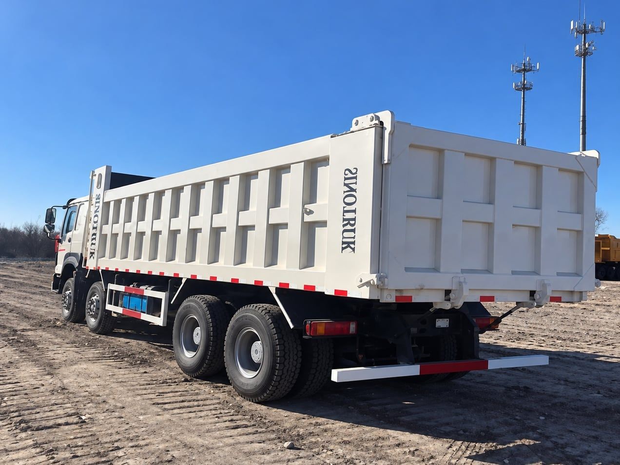 Camion benne Sinotruk HOWO 8×4, vue de trois quarts arrière, toute la longueur de la benne blanche et les quatre essieux visibles