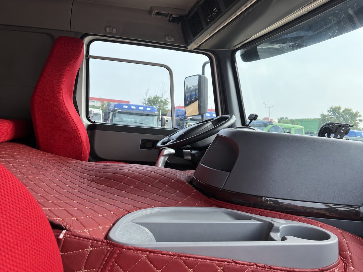 Camion benne Sinotruk HOWO 8×4, intérieur de la cabine : volant à gauche, sellerie rouge matelassée et tableau de bord