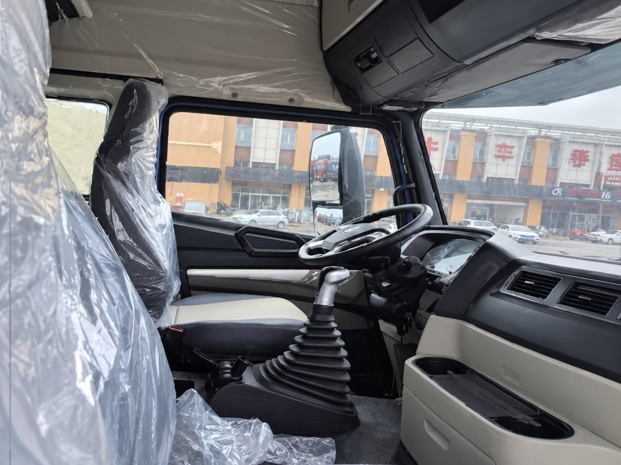 Tracteur routier Sinotruk HOWO NX 6×4, intérieur de la cabine : volant à gauche, tableau de bord et levier de vitesses, sièges encore sous leur emballage de livraison
