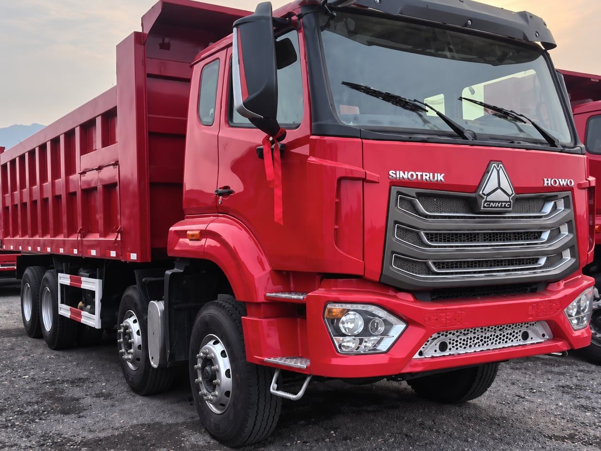 Camion benne Sinotruk HOWO NX 8×4, vue de trois quarts avant dans le parc, cabine et benne rouges